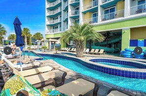 Un espace piscine d’hôtel doté de plusieurs niveaux de balcons, de chaises longues et d’un toboggan aquatique.