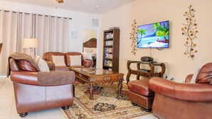 Un salon avec des canapés en cuir, une table basse, une bibliothèque, un téléviseur et un ventilateur de plafond.