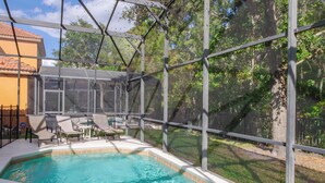 Une piscine dotée d’une enceinte en verre, entourée de chaises longues et d’un espace patio couvert.
