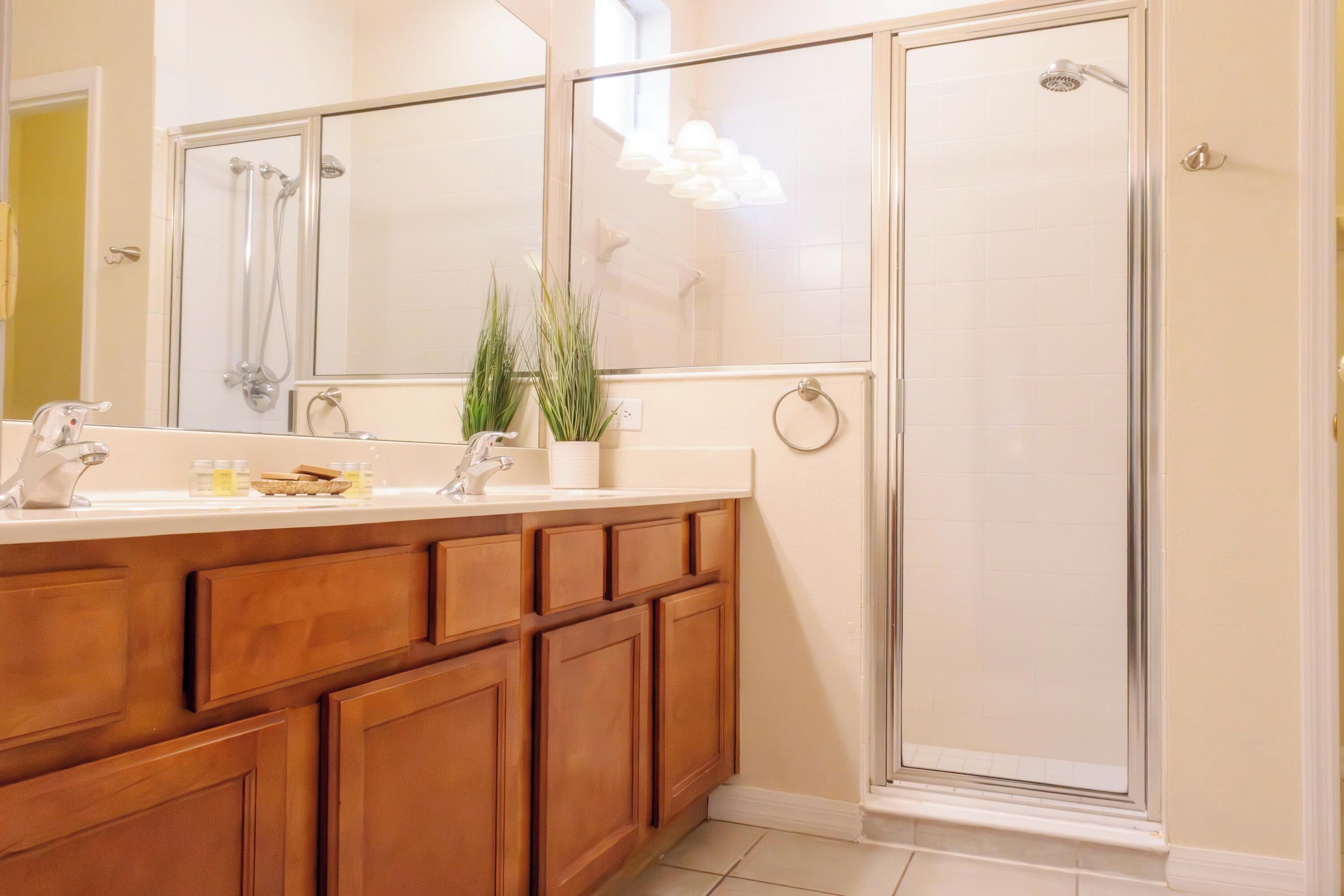 A bathroom with a wooden vanity, a large mirror, and a glass-enclosed shower.