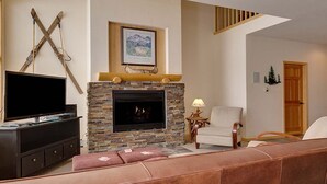 A living room with a stone fireplace, a mounted TV, and a cozy seating area.