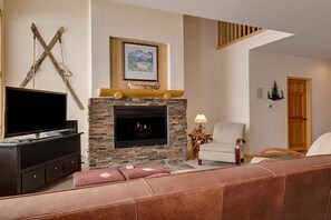 A living room with a stone fireplace, a mounted TV, and a cozy seating area. - True Ski in/Out, Fireplace, Private Hot Tub, Mountain Views, Garage, Peaceful (Breckenridge)