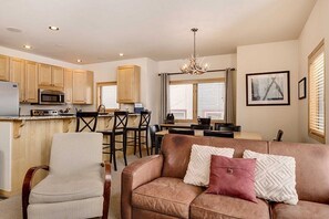 A spacious living area with a leather sofa, a dining table, and a kitchen in the background. - True Ski in/Out, Fireplace, Private Hot Tub, Mountain Views, Garage, Peaceful (Breckenridge)