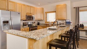 A kitchen with wooden cabinets, granite countertops, stainless steel appliances, and a breakfast bar with chairs.