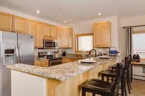 A kitchen with wooden cabinets, granite countertops, stainless steel appliances, and a breakfast bar with chairs. - True Ski in/Out, Fireplace, Private Hot Tub, Mountain Views, Garage, Peaceful (Breckenridge)