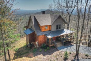 A cabin with a porch, a chimney, and a view of the surrounding landscape.