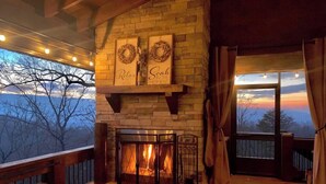 A cozy fireplace area with a stone fireplace, a sofa, and a view of the outdoors. - Tranquility Perch | 3-State Mtn Views + Hot Tub (Murphy)
