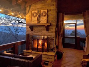 A cozy fireplace area with a stone fireplace, a sofa, and a view of the outdoors. - Tranquility Perch | 3-State Mtn Views + Hot Tub (Murphy)