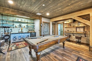 Une table de billard dans une pièce dont le sol est en bois et qui est dotée d’étagères remplies de divers objets.