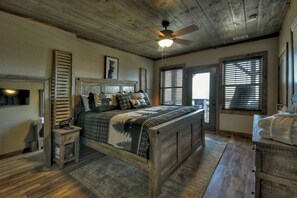 A bedroom with a wooden bed, a nightstand, a ceiling fan, and a window with blinds. - Tranquility Perch | 3-State Mtn Views + Hot Tub (Murphy)