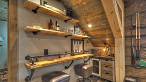 A rustic bar area with wooden shelves, stools, and a hanging light fixture. - Tranquility Perch | 3-State Mtn Views + Hot Tub (Murphy)