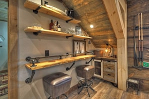 A rustic bar area with wooden shelves, stools, and a hanging light fixture. - Tranquility Perch | 3-State Mtn Views + Hot Tub (Murphy)