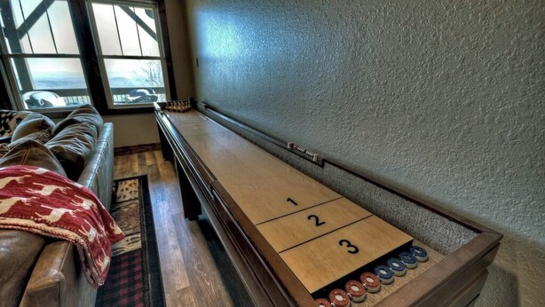 A shuffleboard table with numbered scoring areas and pucks, a leather couch with a blanket, and a window with a view. - Tranquility Perch | 3-State Mtn Views + Hot Tub (Murphy)