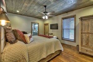 A bedroom with a bed, a ceiling fan, a television, a window with blinds, and a wooden cabinet.