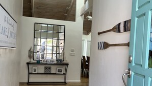 A hallway with wooden flooring, a blue door, a console table with decorative items, and a view into another room.