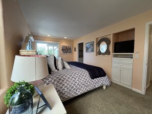 A bedroom with a bed, a TV, a dresser, and a window.