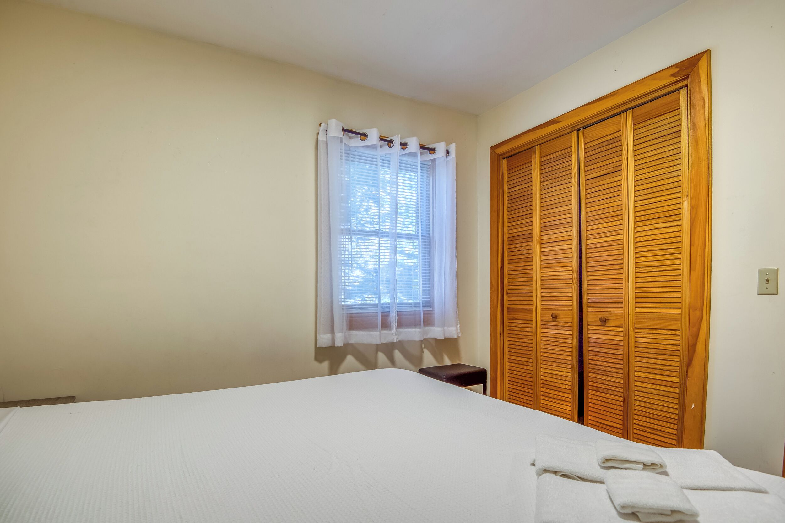 Ein Schlafzimmer mit einem Bett, einem Fenster mit transparenten Vorhängen und einem Holzschrank.