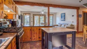 A kitchen with wooden cabinets, a stove, and a dining area with a table. - Relax-Inn - Enjoy this peaceful property along Mingo Loop (Rangeley)