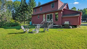 A red house with a front porch, a small deck, and a well-maintained lawn. - Relax-Inn - Enjoy this peaceful property along Mingo Loop (Rangeley)
