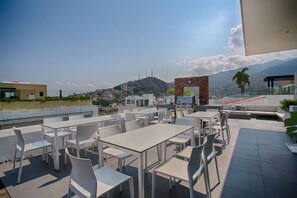 An outdoor seating area with tables and chairs, overlooking a cityscape with buildings and hills.