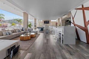 A modern living room with a sofa, coffee table, and TV. There is a kitchen area with a bar and seating.