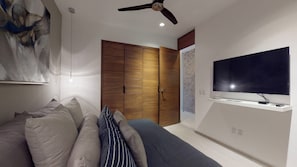 A bedroom with a bed, a ceiling fan, a TV mounted on the wall, and a wooden wardrobe.