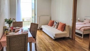 A cozy room with a dining table, wicker chairs, a sofa, and a bed.
