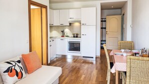 A compact living space with a kitchenette, a dining area with wicker chairs, and a sofa with decorative pillows.