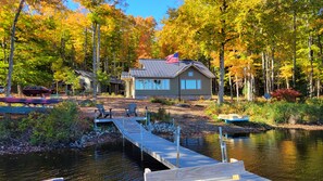 A cabin with a dock extending into a lake, surrounded by autumn foliage.