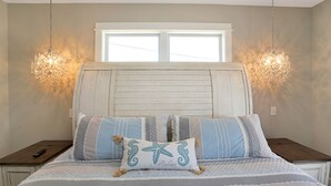 Ein Bett mit gestreifter Bettwäsche, ein Kissen in Form eines Seesterns und zwei Nachttische, auf einem davon eine Fernbedienung.
