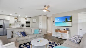 Ein modernes Wohnzimmer mit einer Couch, einem Couchtisch und einem Fernseher, der eine Strandansicht zeigt.