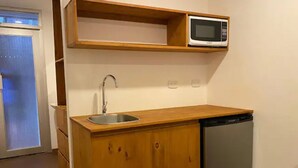 Een kleine keuken met een houten aanrecht, een roestvrijstalen spoelbak, een magnetron en een ingebouwde vaatwasser.