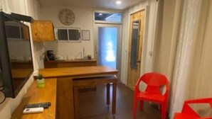 Een knus woongedeelte met een kitchenette, een houten tafel en een rode stoel.