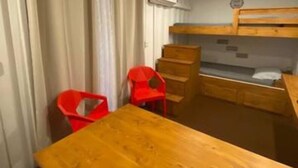 Een kleine kamer met een houten tafel, een stapelbed en een rode stoel.