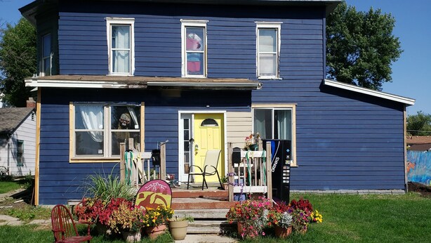 A two-story house with a front porch, a yellow door, and a small garden with potted plants and flowers. - #3 Bohemian Rest Place  (Watertown)
