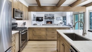 A modern kitchen with wooden cabinets, stainless steel appliances, a stone fireplace, and a large window. - 1 Block from Main Street, Free Shuttle, Walk To Gondola, Nightlife, Shopping (Breckenridge)