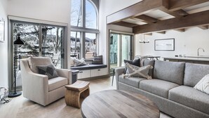 A spacious living area with a large window, a cozy sofa, a round coffee table, and a built-in bench with a view of the outdoors. - 1 Block from Main Street, Free Shuttle, Walk To Gondola, Nightlife, Shopping (Breckenridge)