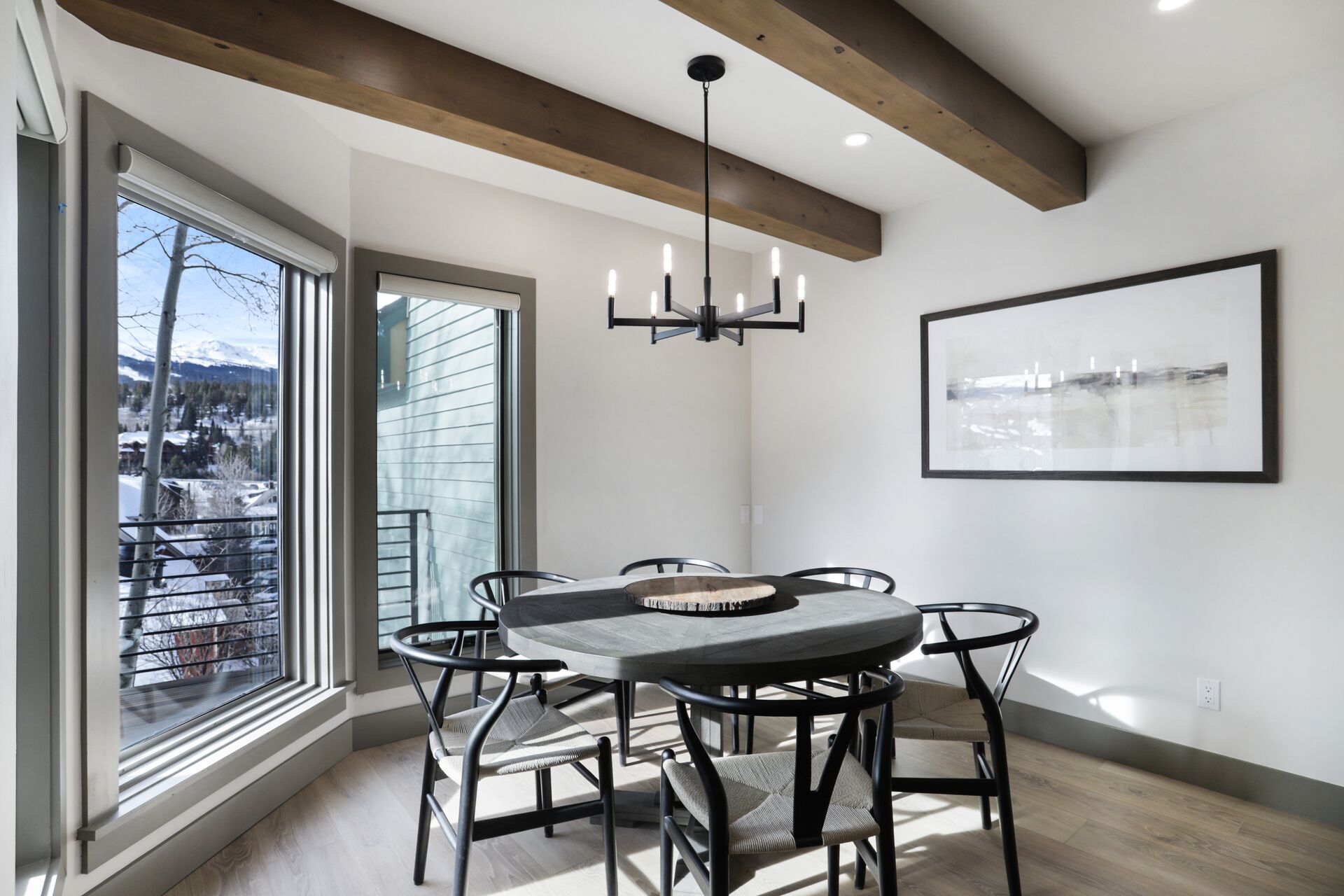 Un coin repas avec une table ronde, des chaises noires, un lustre et un tableau abstrait encadré accroché au mur.