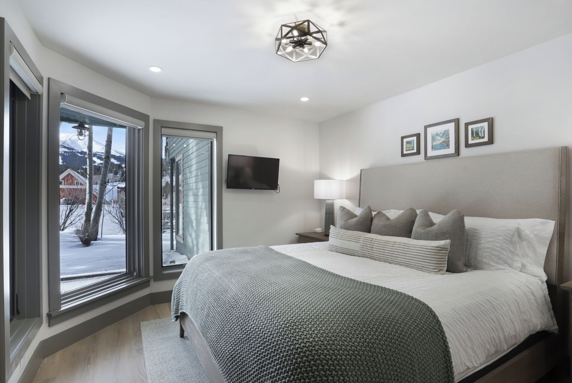 Un dormitorio moderno con una cama grande, un televisor y vistas a un paisaje nevado a través de una puerta corrediza de vidrio.