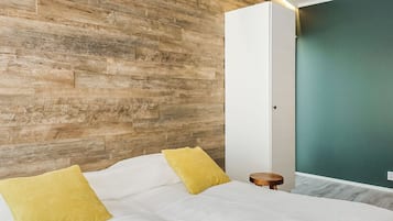 A bedroom with a wooden wall, a bed with white bedding and two yellow pillows, a small wooden stool, and a green accent wall.