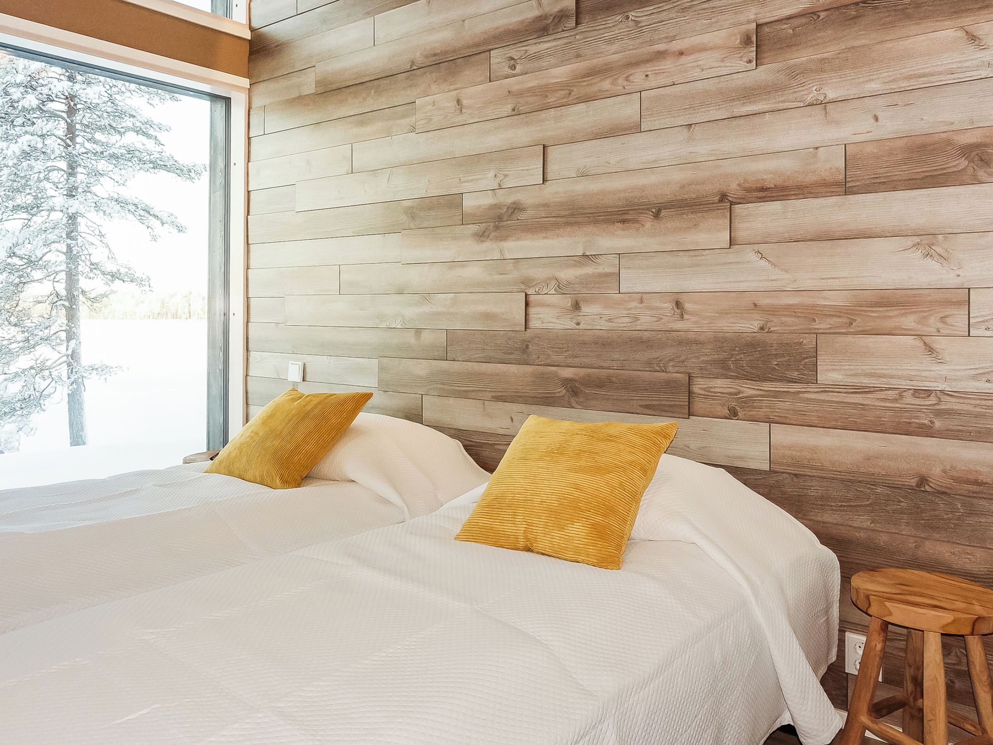 Un dormitorio con cama, dos almohadas, cabecera de madera y ventana con vistas a árboles.