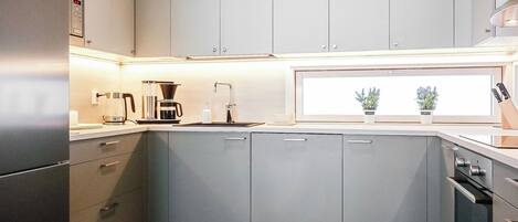 A modern kitchen with grey cabinets, a built-in oven, and a window with potted plants.
