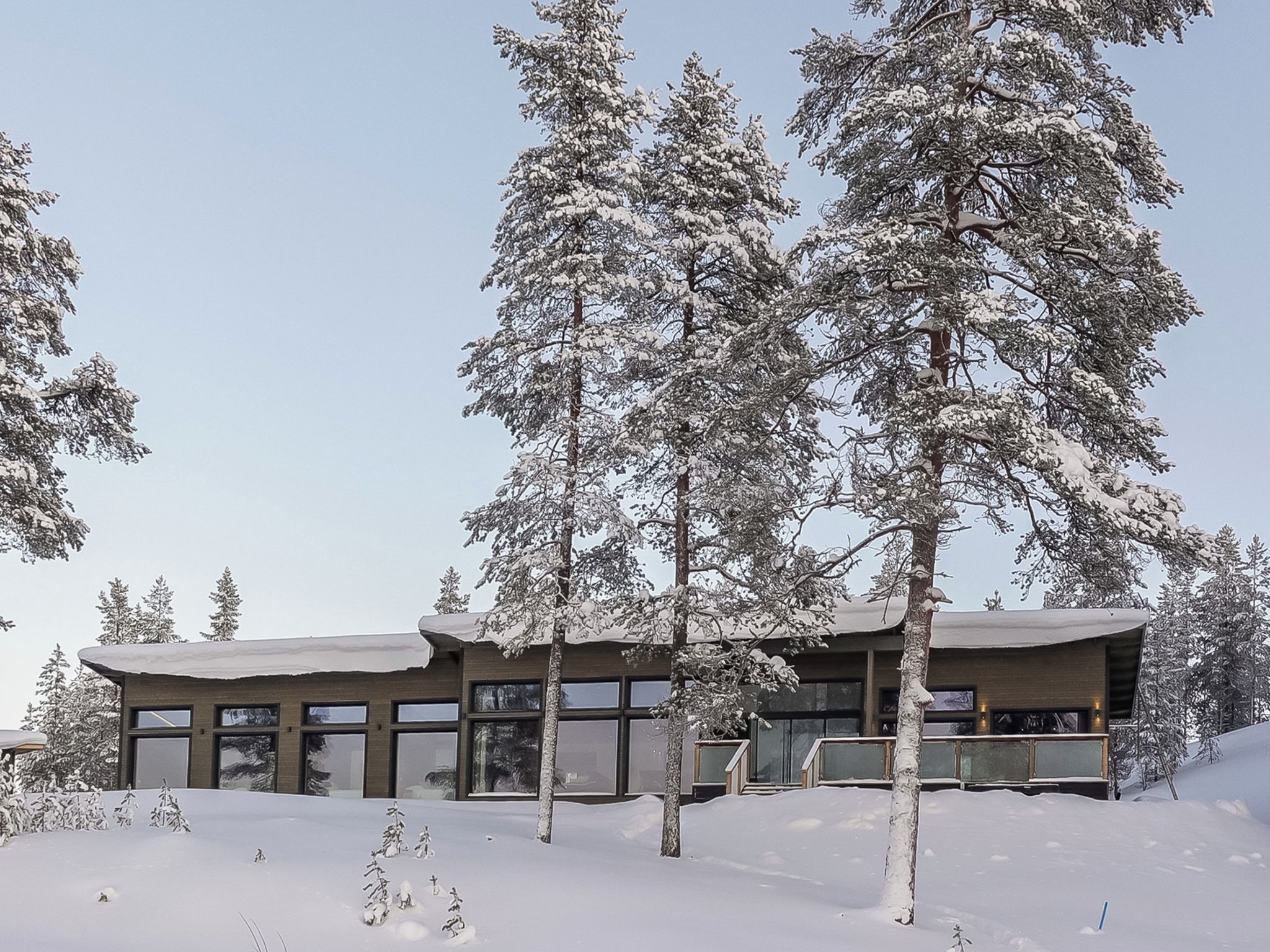 A modern building with large windows and a flat roof, surrounded by snow-covered trees.