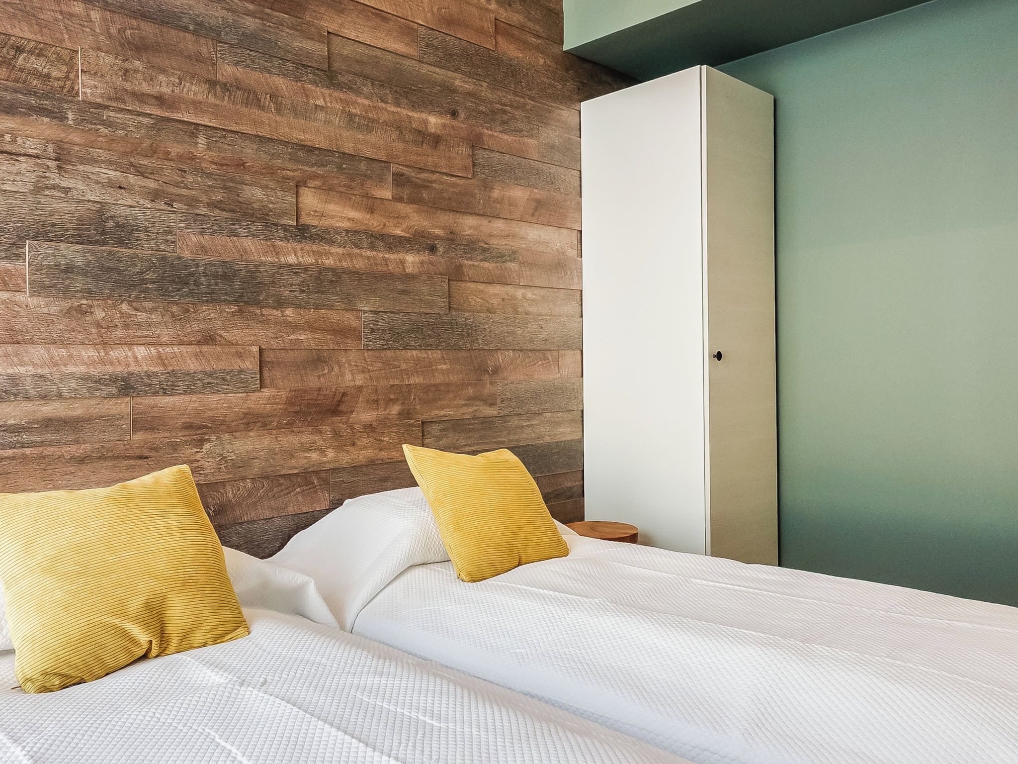 Une chambre avec un mur en bois, un lit avec une literie blanche et une porte verte.