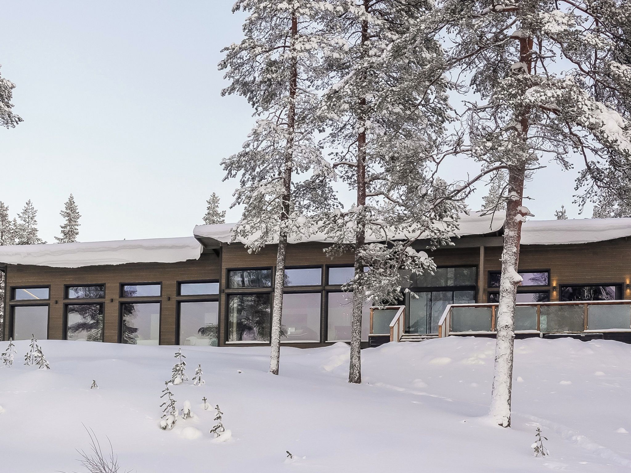A building with large windows and a snow-covered roof, surrounded by snow-laden trees.