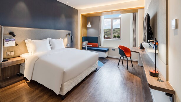 Camera d'albergo moderna con un letto grande, una scrivania con sedia, una televisione e una finestra vista colline.
