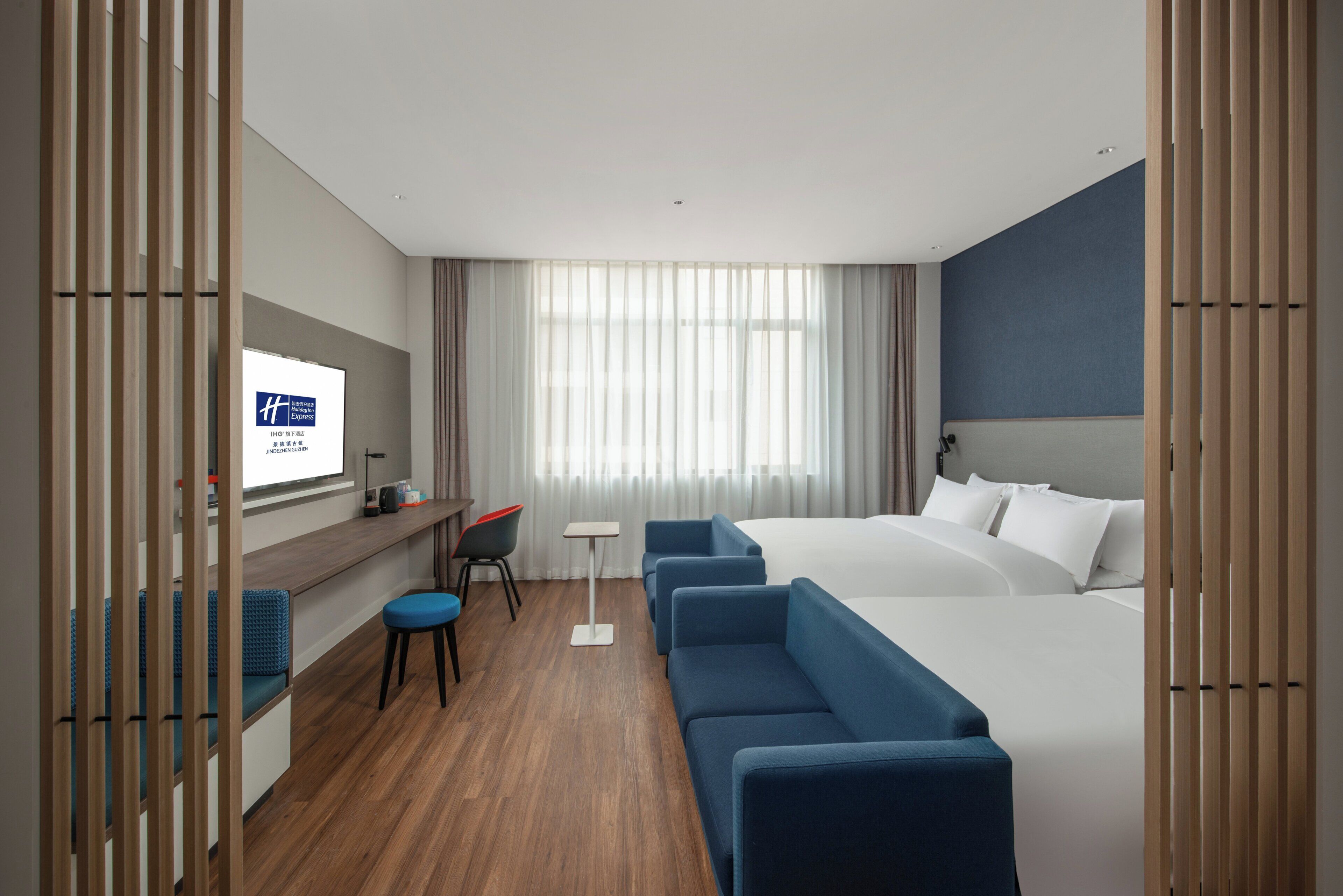 A hotel room with a large bed, a desk with a chair, a small table, and a TV on the wall.