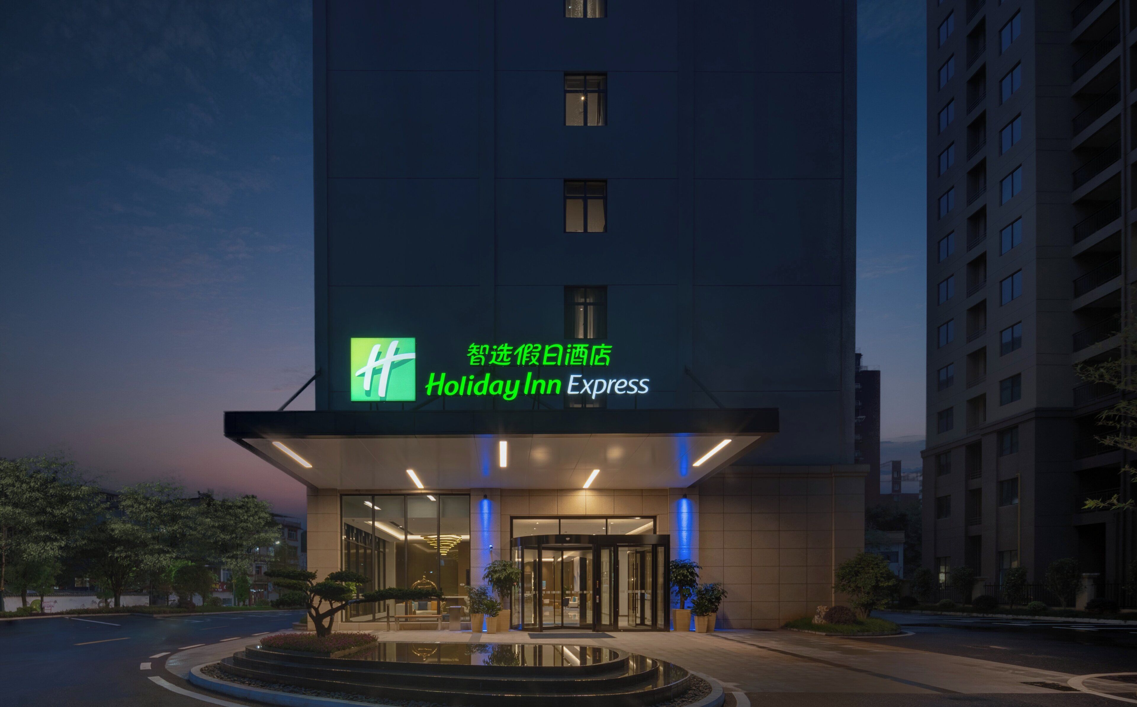 A Holiday Inn Express hotel entrance with a glass facade, a revolving door, and a small water feature in front.