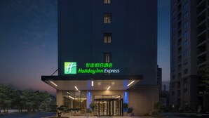 A Holiday Inn Express hotel entrance with a glass facade, a revolving door, and a small water feature in front. - Holiday Inn Express Jingdezhen Ancient Town by IHG (Jingdezhen)
