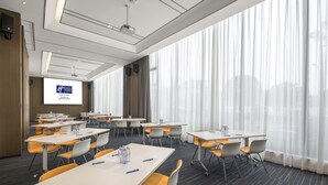 Una sala conferenze con tavoli, sedie, uno schermo per proiettore e ampie finestre con tende.